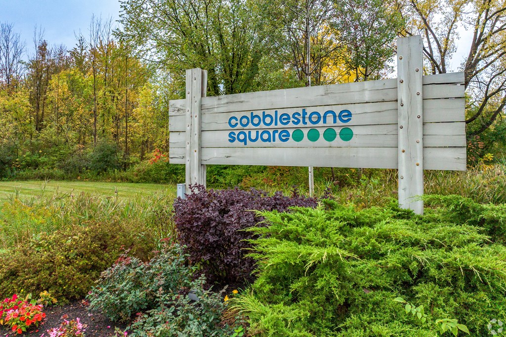 A wooden sign that says Cobblestone Square stands in front of a field of flowers.