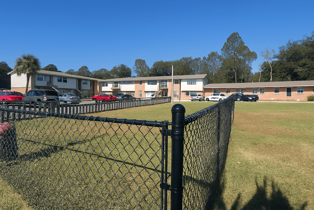 A black fence in front of a building with cars parked in the background.