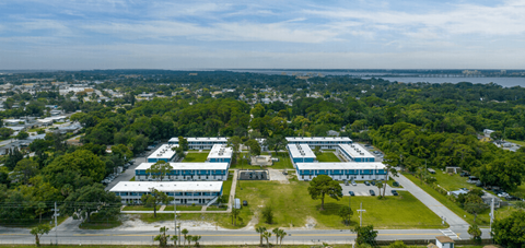 an aerial view of three buildings with trees and a body of water in the background