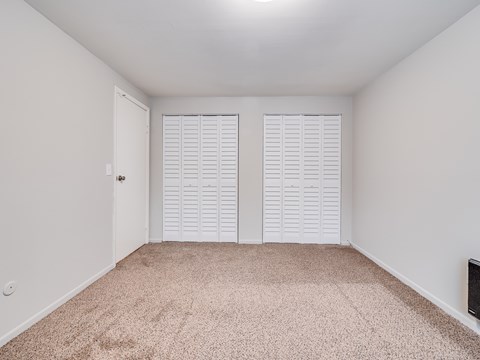 A room with white walls and a carpeted floor with two closets.