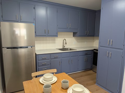 A kitchen with blue cabinets and a stainless steel refrigerator.