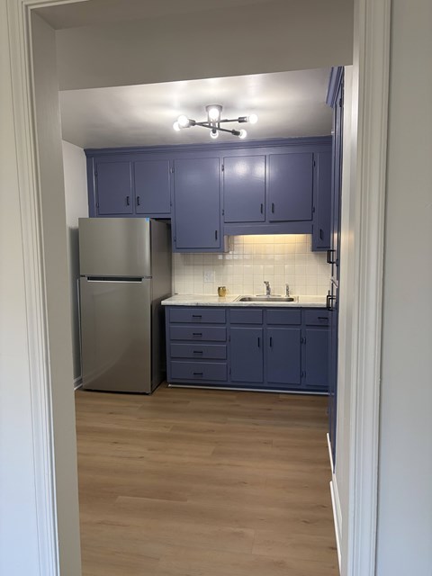 A kitchen with a refrigerator, sink, and cabinets.