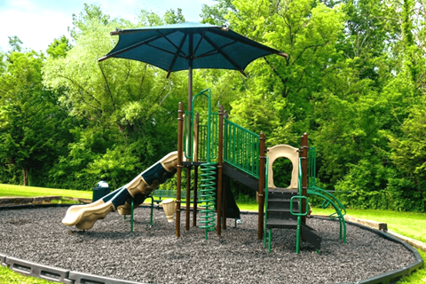 A playground with a green umbrella and a slide.