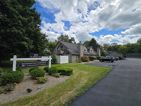 A sign for Brookside East Apartments is in front of a house.
