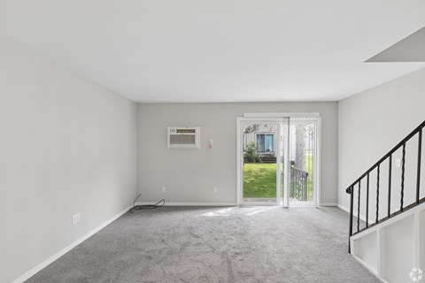 A spacious room with a carpeted floor and a staircase on the right side.