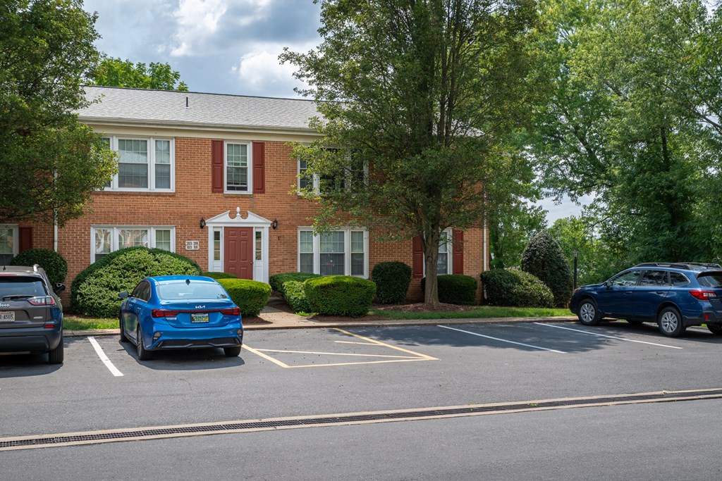 A blue car is parked in a parking lot in front of a red brick building.