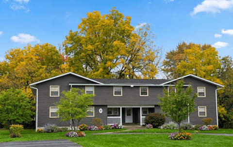 A grey house with a white porch and a tree in front.