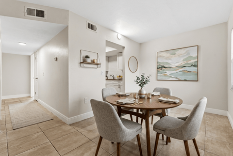 A dining room with a table set for two and a painting on the wall.