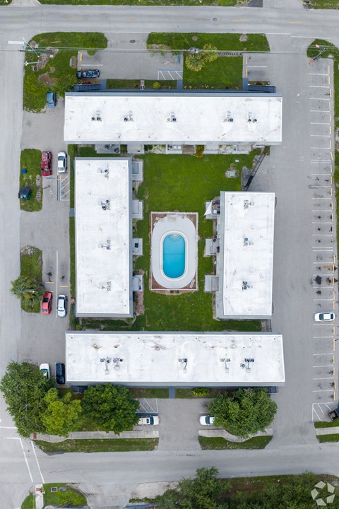 A swimming pool is located in the middle of a grassy area surrounded by buildings.