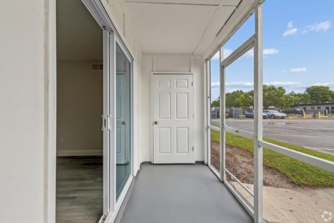 A white door is open to a balcony with a view of a parking lot and trees.