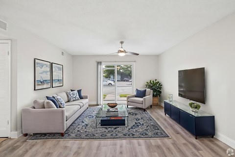 A living room with a grey couch, a coffee table, and a flat screen TV mounted on the wall.