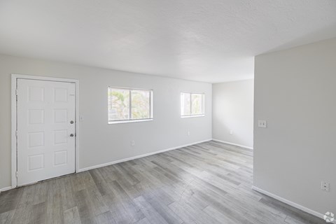 A room with a white door and two windows with wooden flooring.