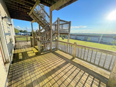 A wooden deck with a staircase leading to a balcony overlooking a grassy area.