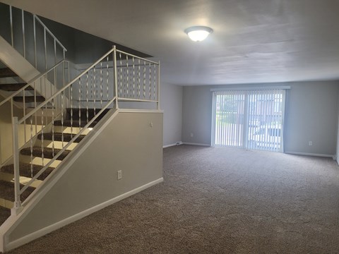 A carpeted room with a staircase and a window.