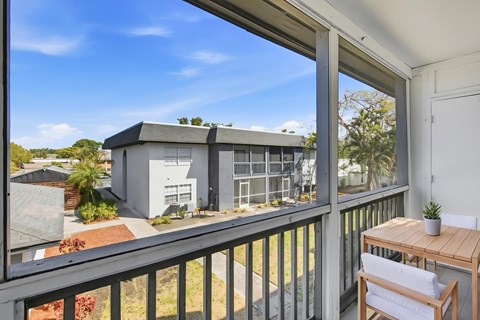 A balcony with a table and chairs overlooks a building and a garden.
