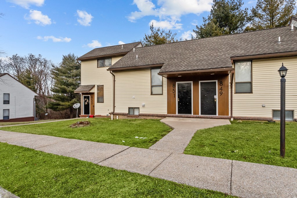 A house with a brown roof and tan siding has a white garage door and a brown door.