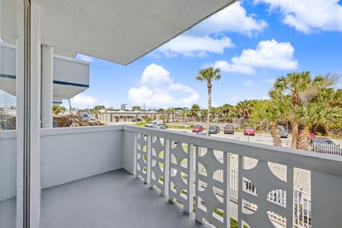 A balcony with a white railing overlooks a parking lot and palm trees.