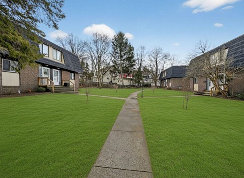 A grassy area with a concrete pathway leading to a building with a solar panel on the roof.