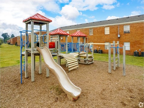 a playground with a slide and chairs in front of a building