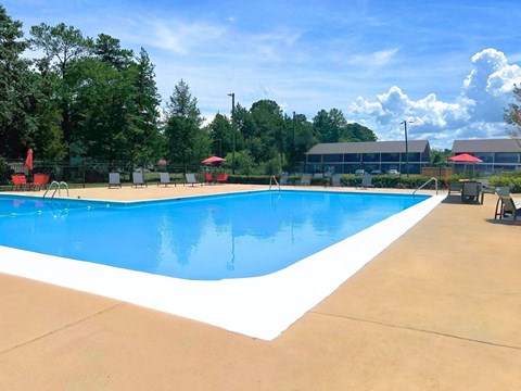 a swimming pool with chairs around it and trees in the background