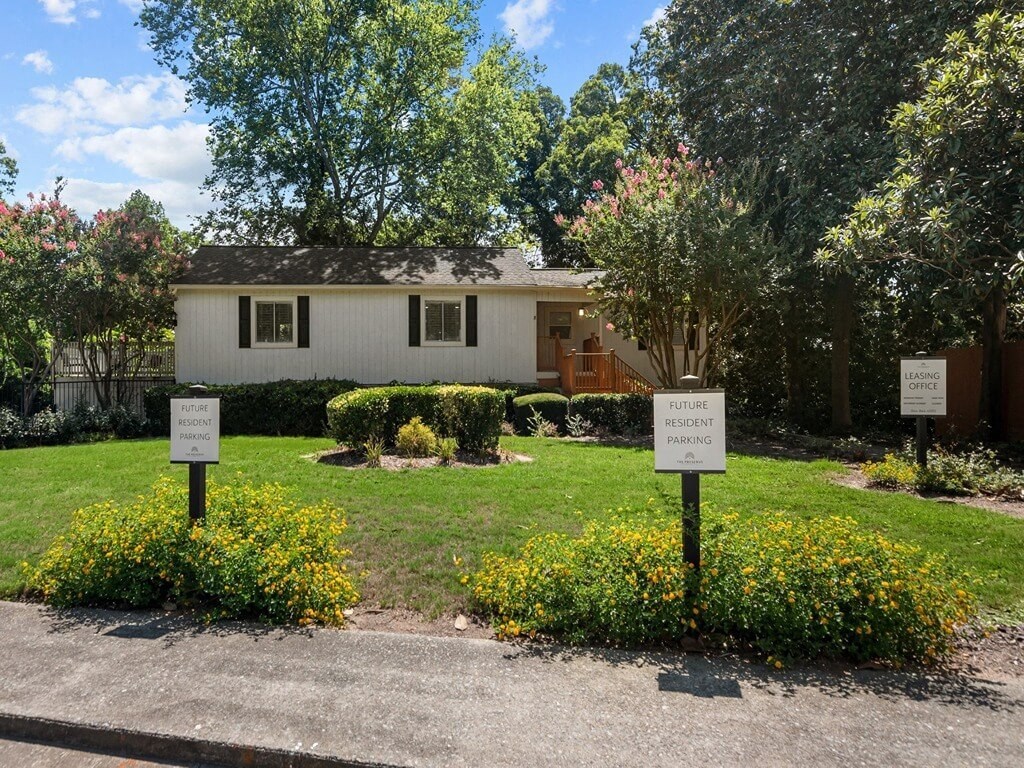 three signs in front of a white house with a lawn and flowers