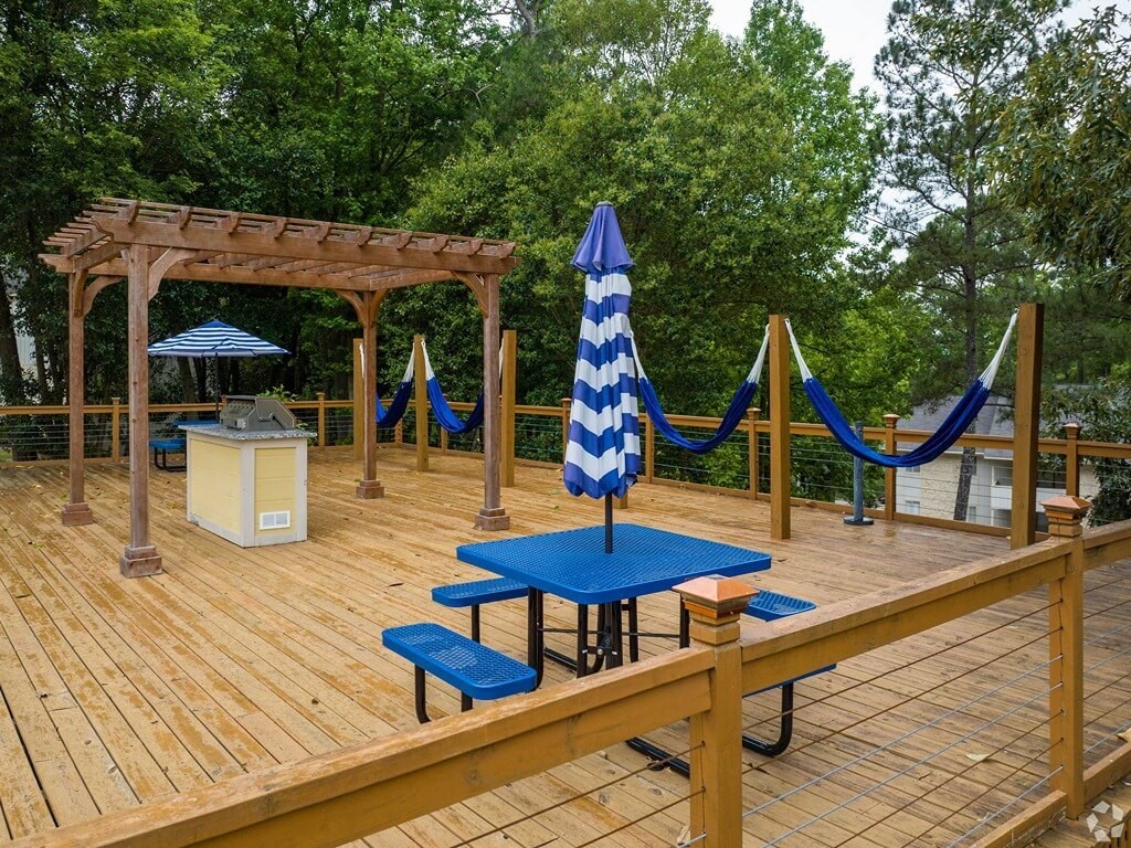 a wooden deck with benches and a table with an umbrella and hammocks