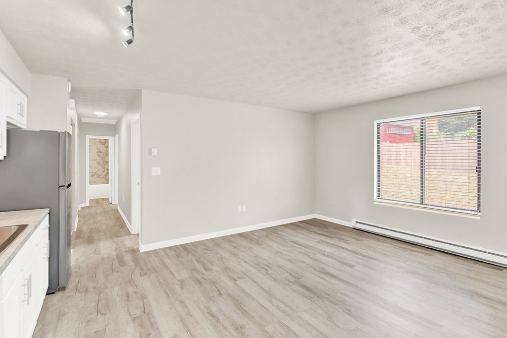 the living room and kitchen of an apartment with white walls and wood flooring