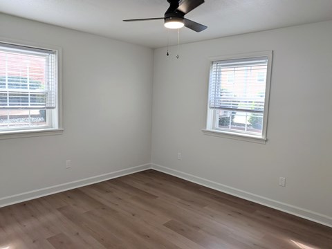 A room with a ceiling fan and two windows.