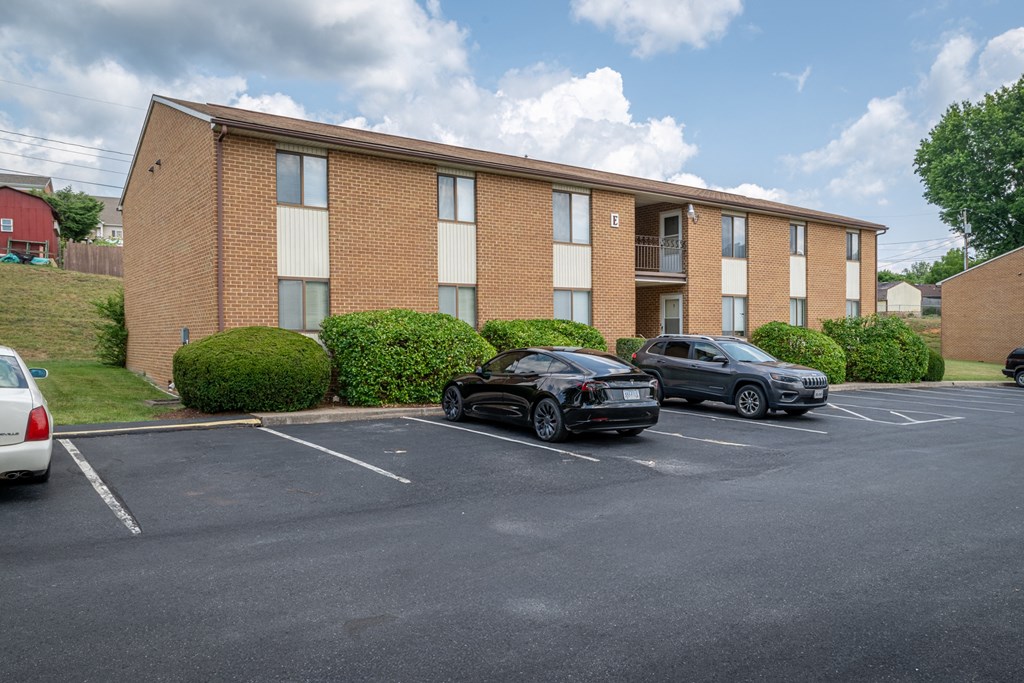 A black car is parked in a parking lot in front of a brick building.
