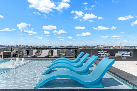 A pool with blue chairs and a cityscape in the background.