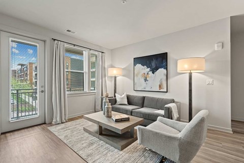 A living room with a grey couch, a grey armchair, a coffee table, and a painting on the wall.