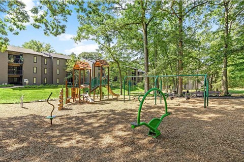 A playground with swings and a slide on brown sandy ground.