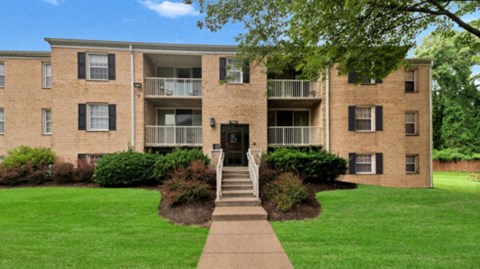 an apartment building with a green lawn and a sidewalk