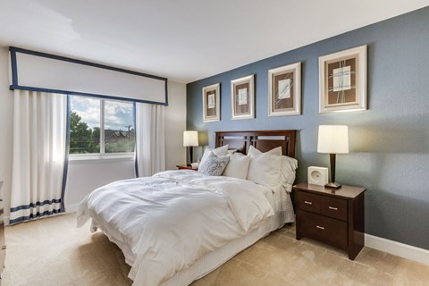 A bedroom with a large bed, a nightstand with a lamp, and pictures on the wall.
