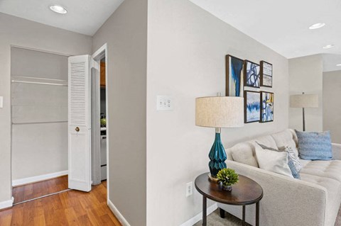 A living room with a white couch, a table with a blue lamp, and pictures on the wall.