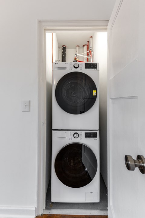 A white washing machine is in a small space between a door and a wall.
