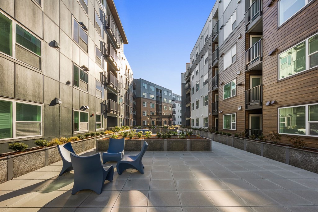 A sunny day in a courtyard with a bench and a building in the background.