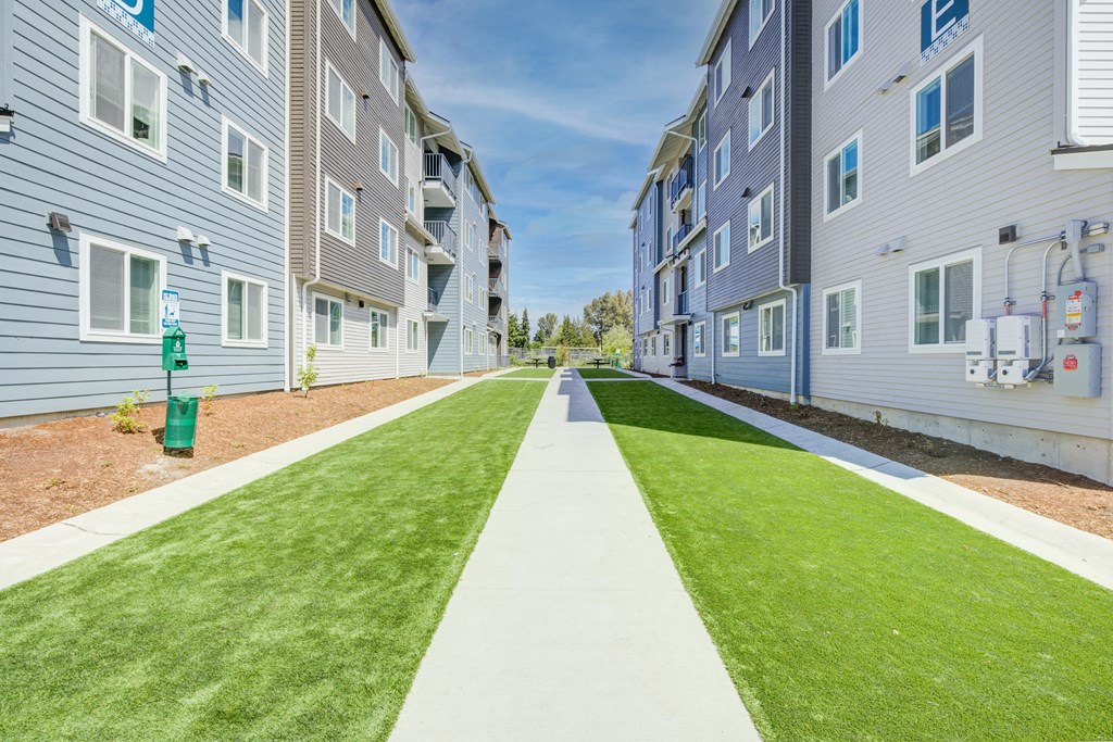 an empty sidewalk in front of an apartment building with grass