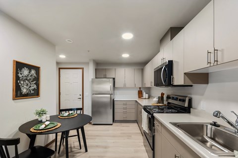 A modern kitchen with a round table and chairs, a fridge, a microwave, and a sink.