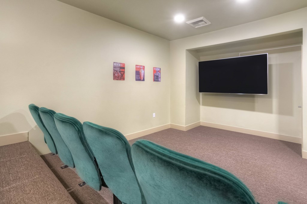 A room with a row of green chairs and a black screen on the wall.