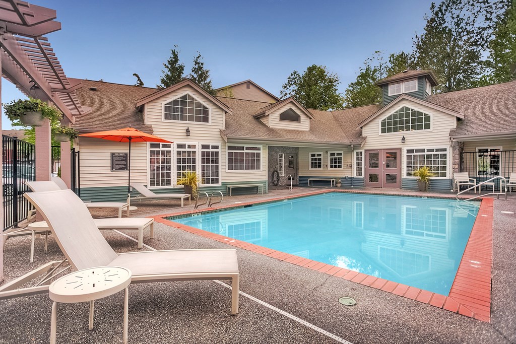 A pool and lounge chairs are in front of a house.
