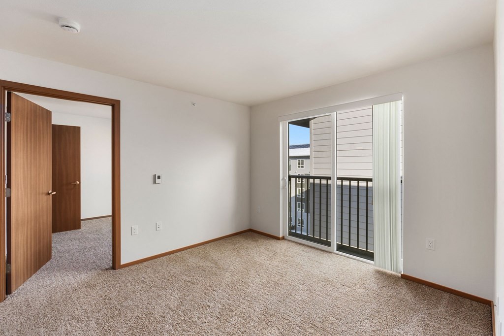 A room with a carpeted floor and a sliding glass door leading to a balcony.