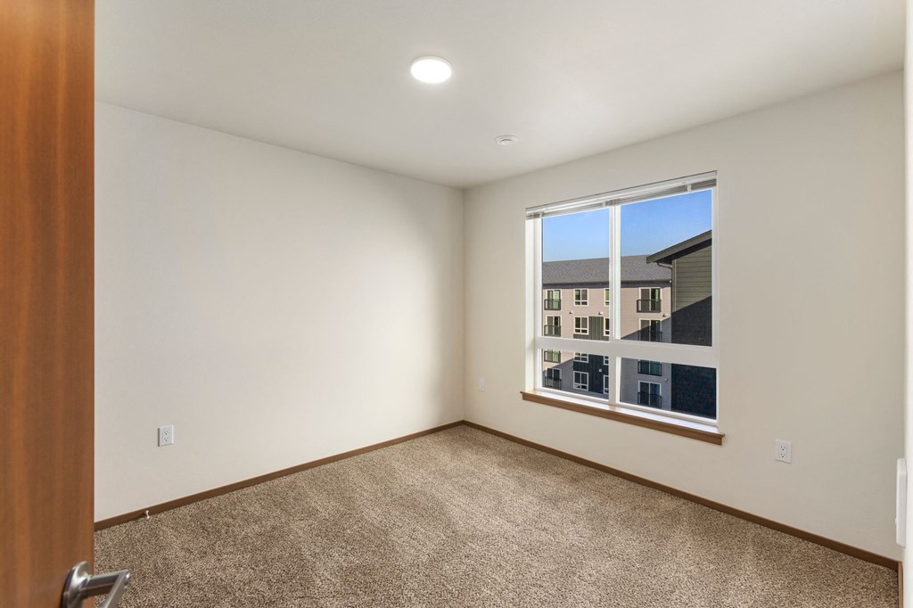 A room with a carpeted floor and a window showing a view of other buildings.