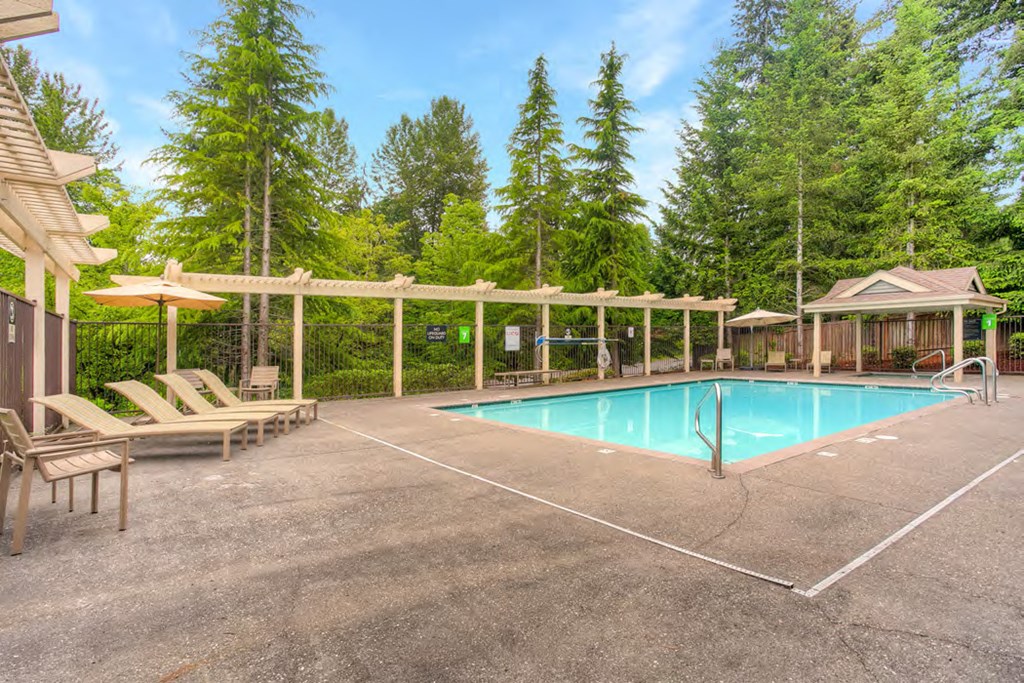 a swimming pool with chairs and umbrellas next to a building and trees
