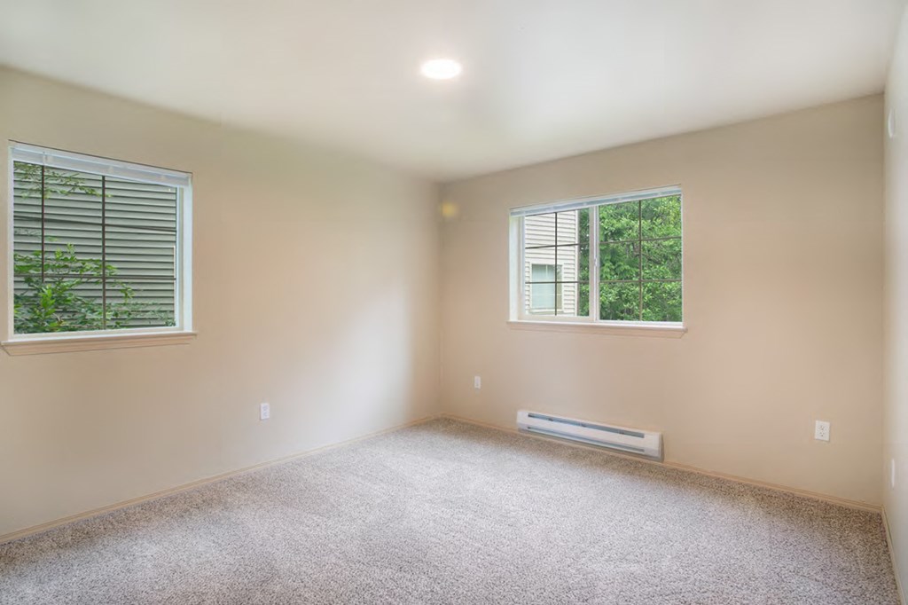 an empty room with two windows and a carpeted floor