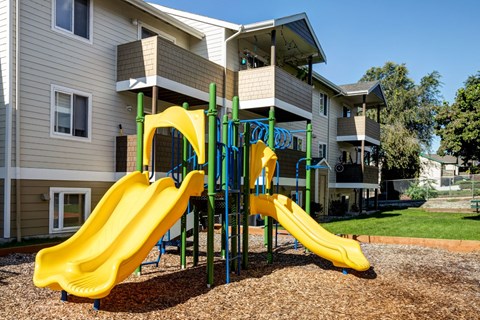 A playground with a yellow slide in front of a building.