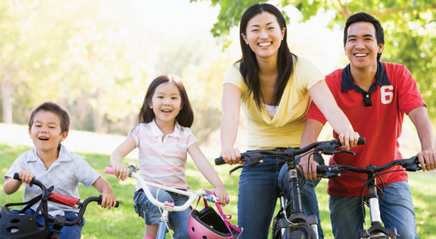 A family of four riding bikes together in a park.