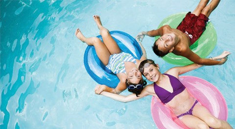 Three people are floating on colorful inner tubes in a pool.