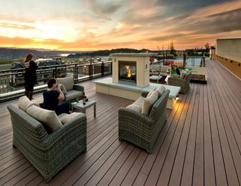 A couple is sitting on a couch on a wooden deck with a fireplace.