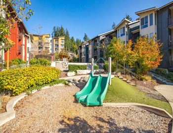 A playground with a green slide in the foreground and apartment buildings in the background.